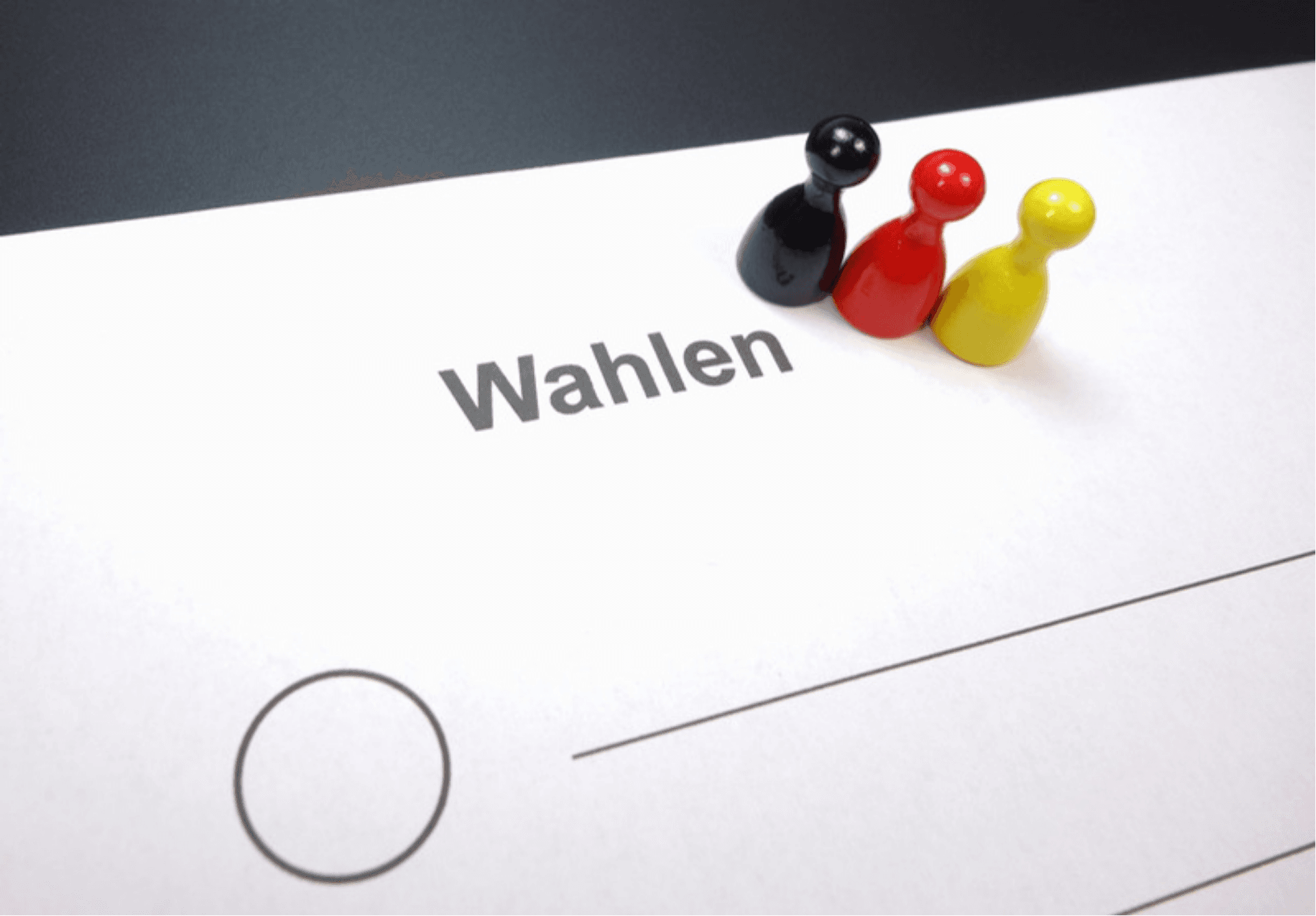 Zettel mit der Überschrift Wahlen, drei (schwarz, rot, gelb) Spielfiguren aneinandergereiht 
