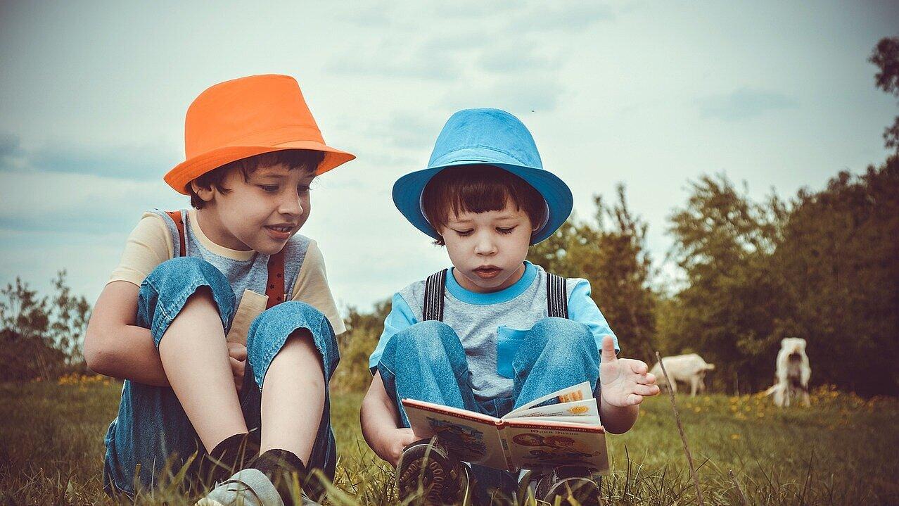 Zwei Jungs sitzen auf einer Wiese und lesen in einem Buch.