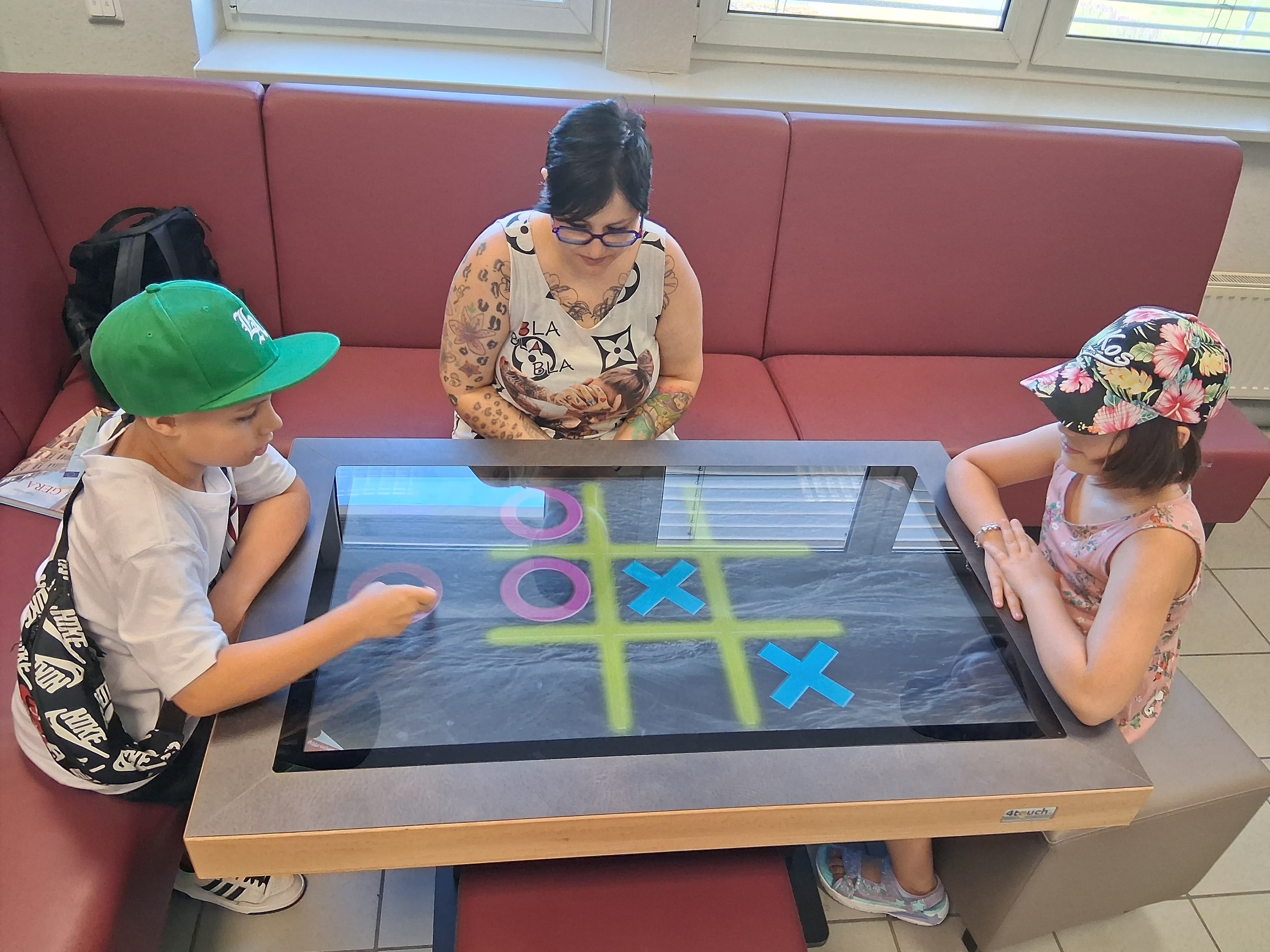 Zwei Kinder und eine Erwachsene, die an einem digitalen Spieltisch ein Spiel ausprobieren. © Stadt Gera