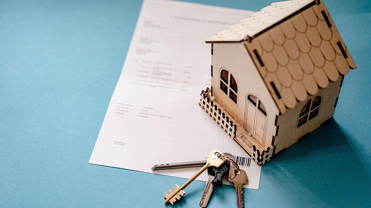 Kaufvertrag mit Schlüssel und kleinem Holzhaus